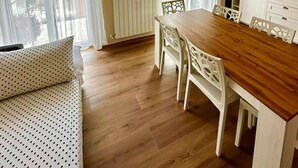 Ein Essbereich mit Holztisch und weißen Stühlen, einem Heizkörper und einer Klimaanlage an der Wand.