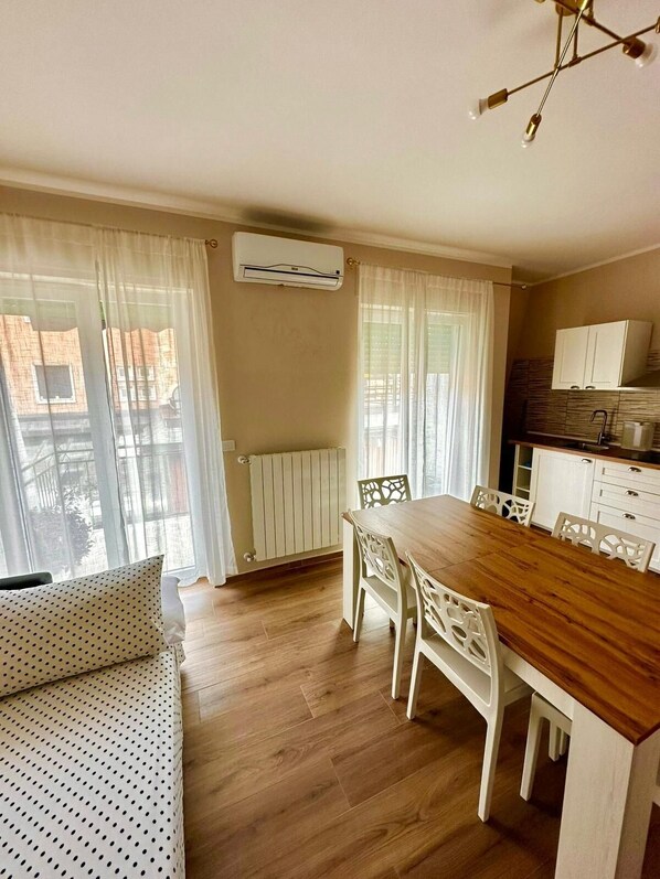 Un coin repas avec une table en bois et des chaises blanches, un radiateur et un appareil de climatisation fixé au mur.
