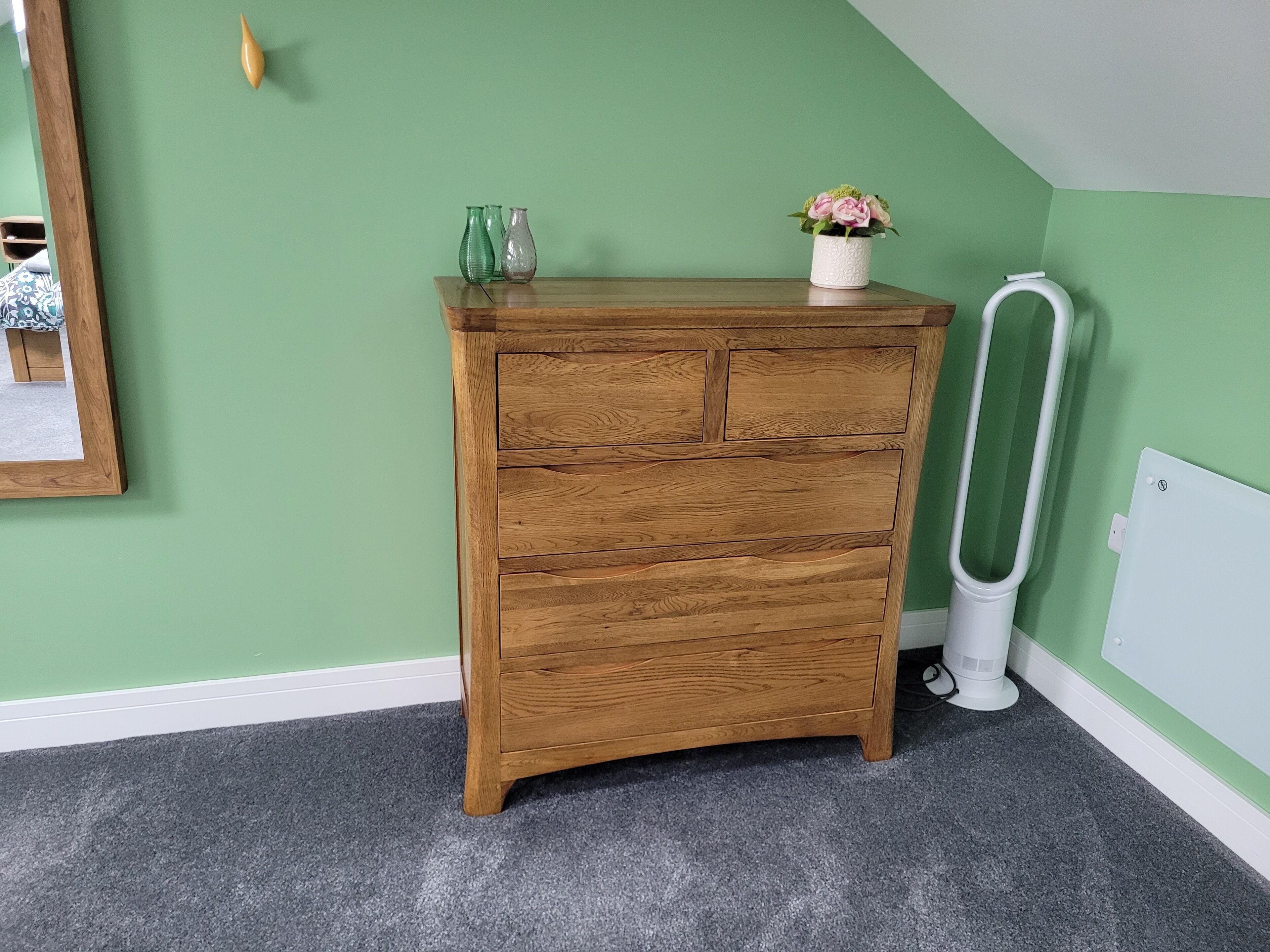 A wooden chest of drawers against a green wall, with a white radiator and a framed picture on the floor.