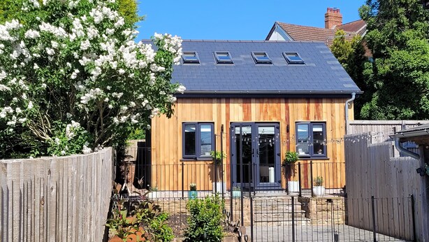 Et moderne hus med facade af træ, flere vinduer og et skråt tag.
