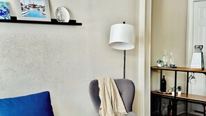 A living room with a blue sofa, a grey armchair with a throw blanket, a floor lamp, and a shelf with decorative items. - Cute and Close to Downtown! Off street parking w/ short walk to Academy/Stadium (Annapolis)
