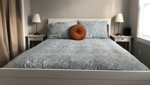 A neatly made bed with patterned bedding, two bedside lamps, a wall-mounted air conditioner, and a window with blinds. - Cute and Close to Downtown! Off street parking w/ short walk to Academy/Stadium (Annapolis)