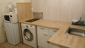 A compact kitchen with a washing machine, microwave, and a sink. - Studio Dans Voûtes (Creissels)