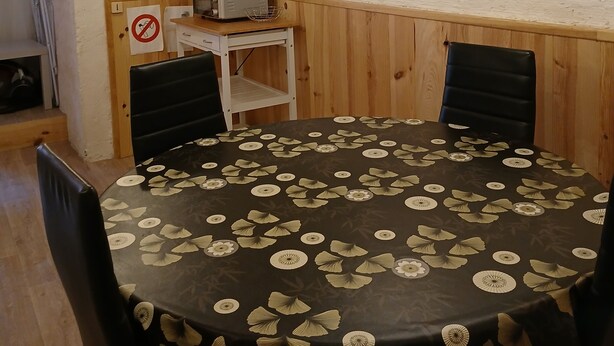 A room with a round table, two chairs, a small desk with a computer, and a wall clock. - Studio Dans Voûtes (Creissels)