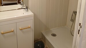 A bathroom with a white sink, a handheld showerhead, and a toilet. There is a trash can and a towel hanging on the wall. - Studio Dans Voûtes (Creissels)