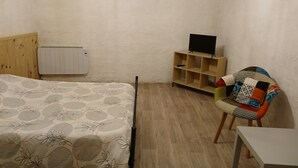 A bedroom with a bed, a wooden chair, a TV on a wooden stand, and a radiator. - Studio Dans Voûtes (Creissels)