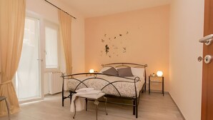 A bedroom with a bed, bedside tables, a chair, a radiator, and a window with curtains. - Il Giardino Degli Agrumi - Roma (Roma)