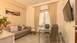 A modern living room with a sofa, a glass dining table, and a TV mounted on the wall. - Il Giardino Degli Agrumi - Roma (Roma)