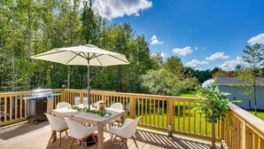 Een houten terras met een tafel, stoelen, een barbecue en een parasol.
