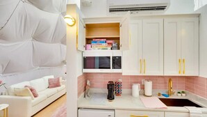 Een compacte keuken met witte kastjes, een ingebouwde magnetron en een klein spoelbakje.