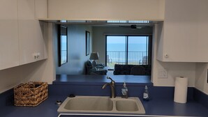 A modern kitchen with a sink, a basket, and a view of a balcony with a chair and a table. - Ocean Front Condo Downtown Cocoa Beach (Cocoa Beach)