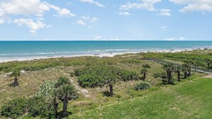 A coastal landscape with a beach, grassy areas, and a wooden boardwalk. - Ocean Front Condo Downtown Cocoa Beach (Cocoa Beach)