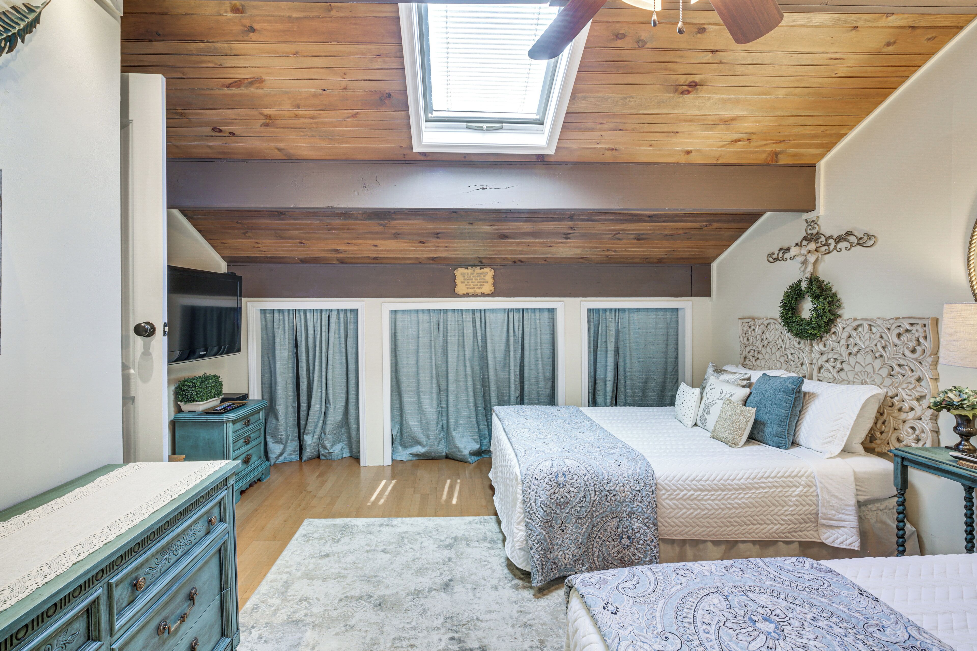 Une chambre avec un plafond en pente, une lucarne, un lit recouvert d’une couvre-lit à motifs, une commode et une table de chevet.
