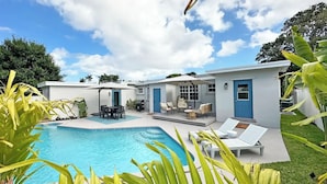 Ein modernes Haus mit Swimmingpool, Gartenmöbeln und einer blauen Tür.