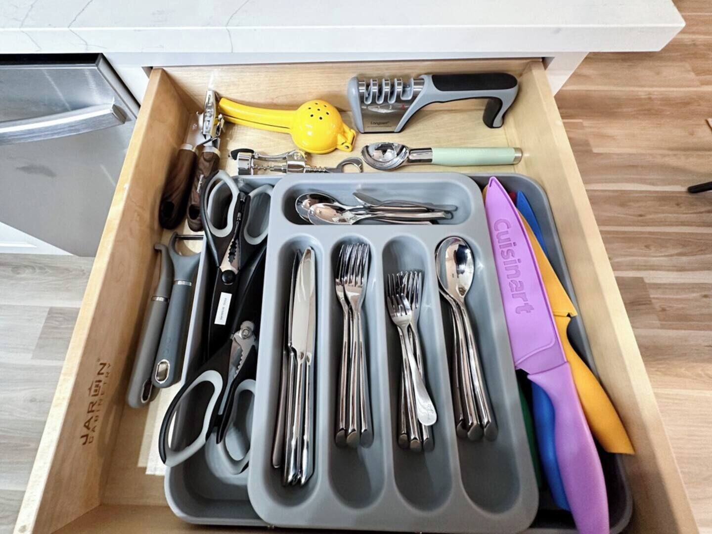 A drawer containing various kitchen utensils and tools, including scissors, a grater, and a yellow colander.