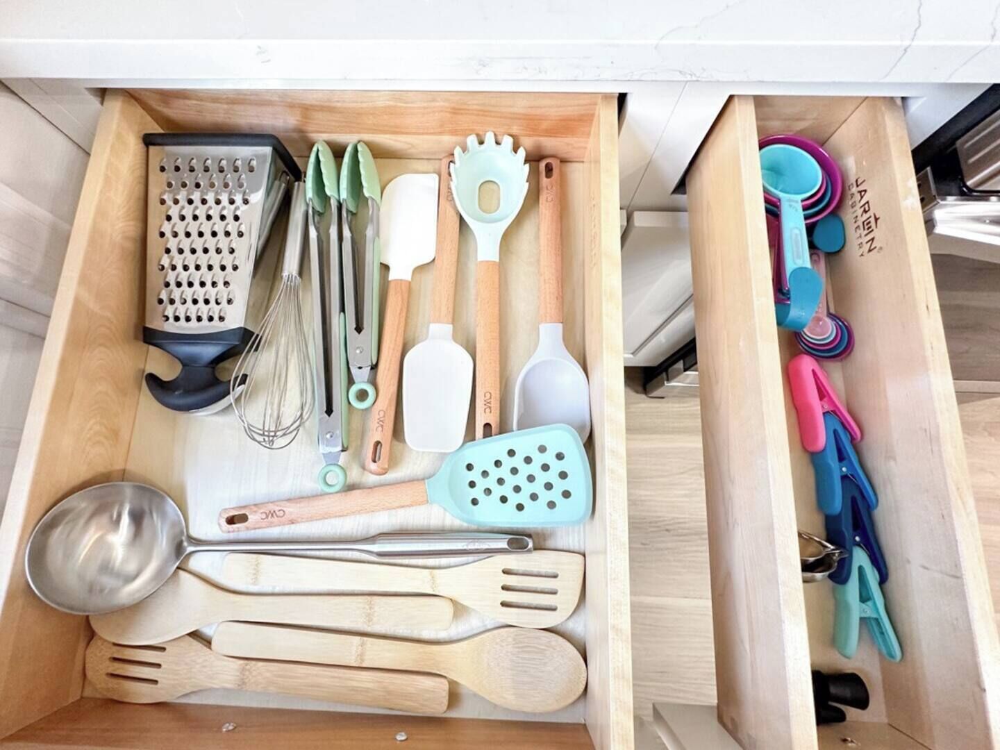 Un cajón con varios utensilios de cocina, incluyendo un rallador, batidores, espátulas y tazas medidoras.