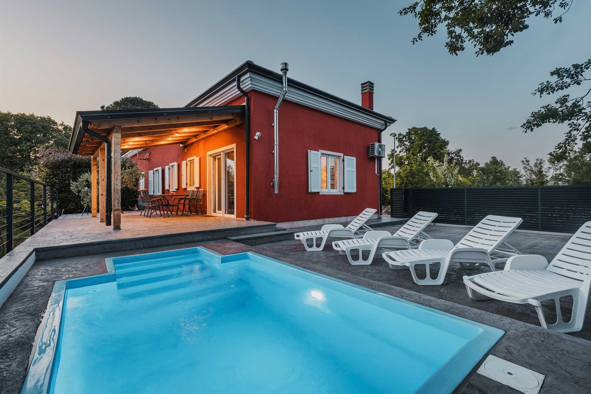 Un edificio rojo con un porche cubierto, piscina y sillas de descanso blancas.