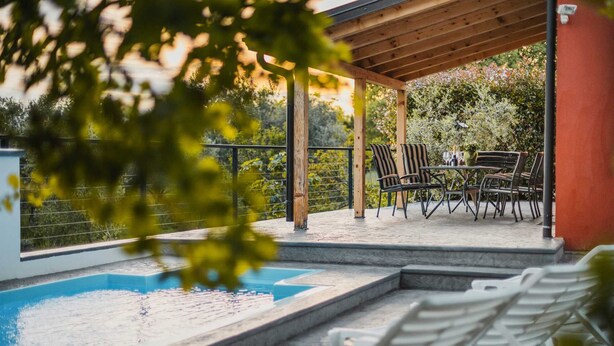 A covered outdoor area with a swimming pool, lounge chairs, and a table with chairs. - Villa Lutoma-2 BD villa with pool and playground (Umag)