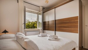 A bedroom with a large bed, a window with curtains, a radiator, and a wooden panel wall. - Villa Lutoma-2 BD villa with pool and playground (Umag)