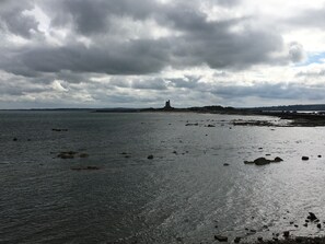 A coastal landscape with a lighthouse, rocky shoreline, and overcast sky.