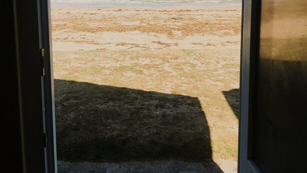 A view through a door to a beach with sand and water.