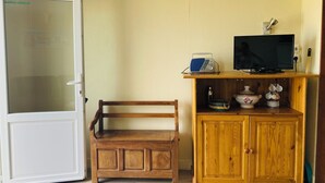A room with a wooden bench, a cabinet with kitchen items, a television, and a door with frosted glass.