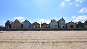 A row of beach houses with a sandy beach in the foreground and a clear sky.