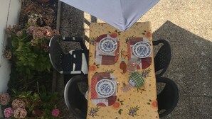 A table set outdoors with a floral tablecloth, two plates, a bottle, and a glass.