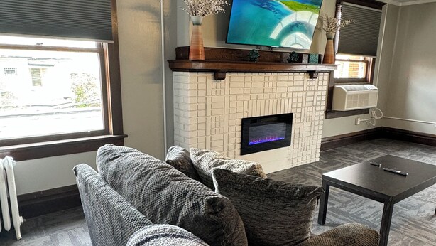 Un soggiorno con camino, una televisione a schermo piatto montata sopra, un divano con una coperta e un tavolino.