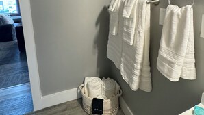 Un bagno con pareti grigie, un lavandino bianco e due asciugamani appesi a un porta-asciugamani. Sul pavimento, un cesto con una borsa nera.