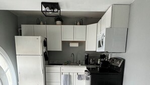 Una cucina compatta con mobili bianchi, un frigorifero, un forno a microonde e una macchina per il caffè.