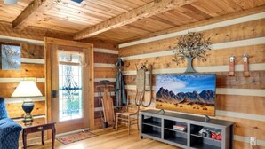 A rustic cabin interior with wooden walls, a wooden ceiling, a television on a stand, and a door with a glass panel.