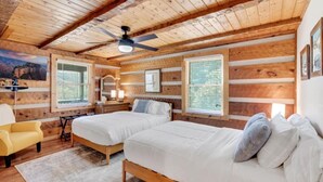 A cabin-style bedroom with two beds, wooden walls, a ceiling fan, and large windows.