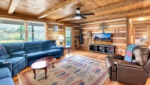 A log cabin interior with a blue sectional sofa, a leather recliner, a wooden coffee table, and a television on a wooden stand.