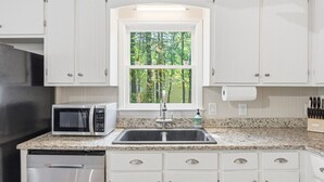 A kitchen with white cabinets, a built-in microwave, a stainless steel sink, and a window with a view of trees. - Charming 4BR ★ Family-Friendly ★ w/Backyard ★ (Raleigh)