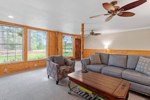 A spacious room with large windows, a ceiling fan, a sofa, a patterned armchair, and a coffee table.