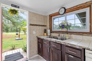 A kitchen with a window, a clock, and a garden view.