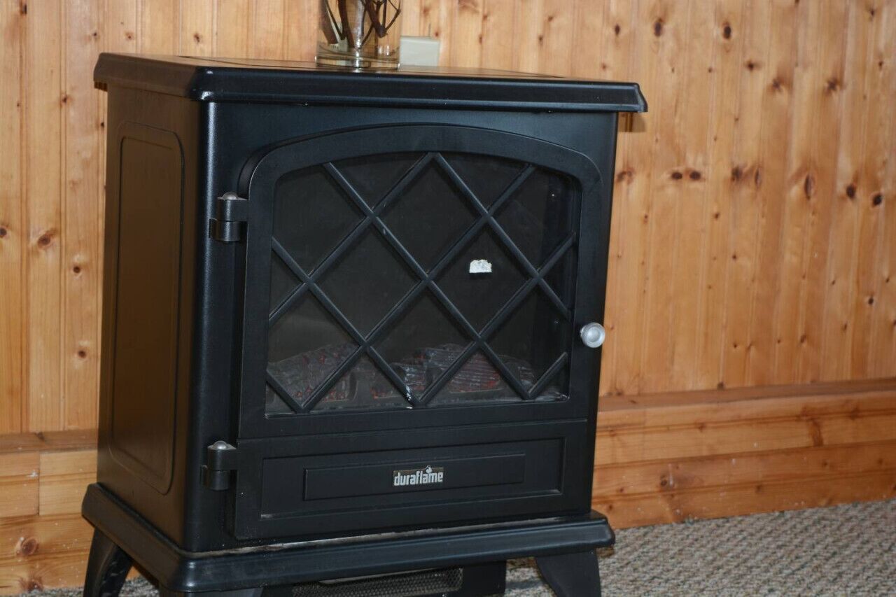 Ein schwarzer Kaminofen mit Glastür, beschriftet 'duraflame', vor einer Holzwand.