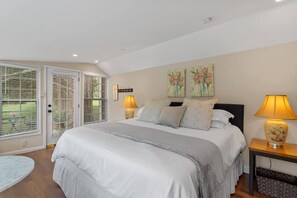 A bedroom with a bed, two bedside lamps, a nightstand, a small table, and a view of the outdoors through a door.