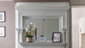 A white fireplace with a mirror above it, flanked by two columns. There is a framed picture on the mantel and a potted plant with white flowers. - In the heart of Adams Morgan | Vintage Charm (Washington)