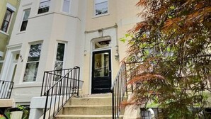 A multi-story building with a central entrance, a staircase with black railings, and a tree with autumn leaves in the foreground. - In the heart of Adams Morgan | Vintage Charm (Washington)