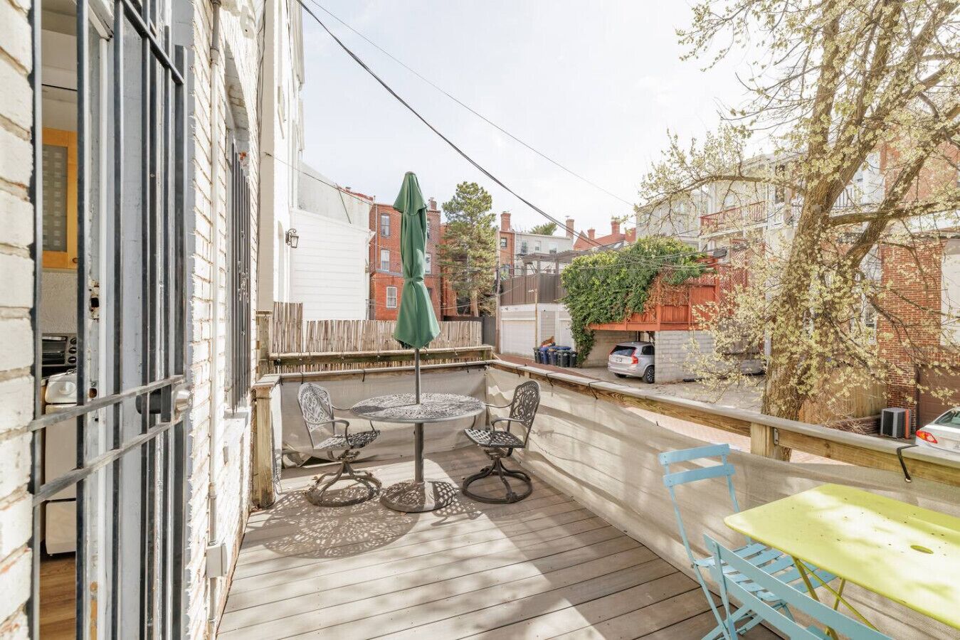 Une terrasse en bois avec une table ronde et des chaises, un parasol vert et une table jaune.