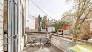 A wooden deck with a round table and chairs, a green umbrella, and a yellow table. - In the heart of Adams Morgan | Vintage Charm (Washington)
