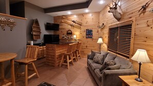 A cozy cabin-style room with a bar area, wooden walls, and a mounted deer head.
