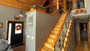 A wooden interior with a staircase, a black door with a wreath, and a sign with rules.