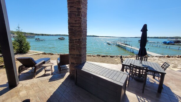 A wooden deck with outdoor seating, a brick pillar, and a view of a lake with boats and docks.