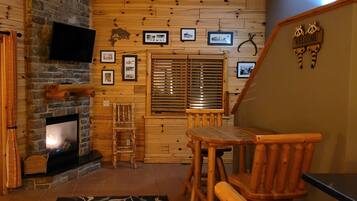 L’intérieur chaleureux d’un chalet avec une cheminée, des murs en bois, un coin repas et une pancarte « Bienvenue ».