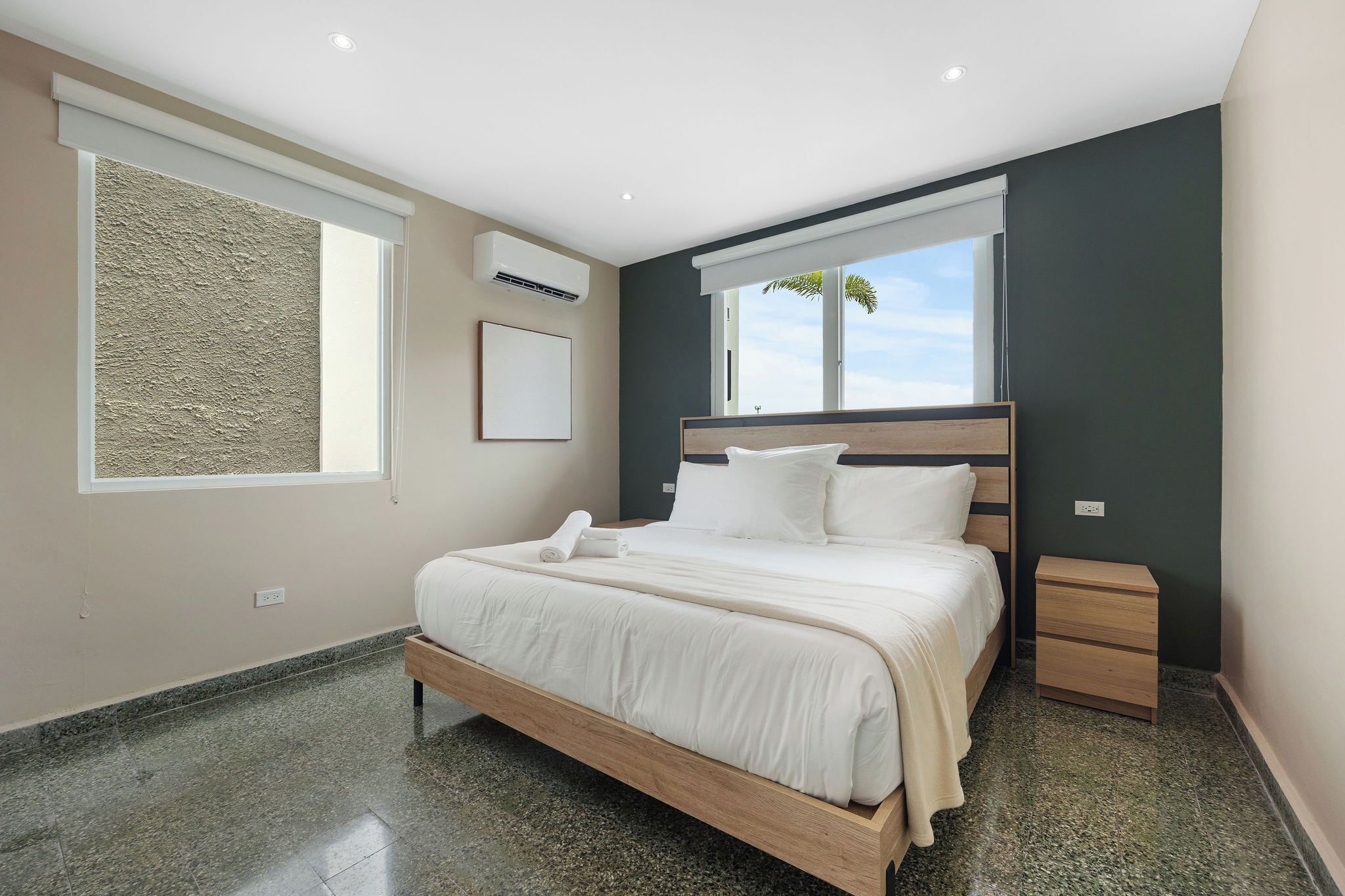 Un dormitorio moderno con una cama de madera, una mesita de noche, un ventanal con vistas y un equipo de aire acondicionado.