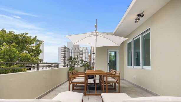 Ein Balkon mit Holztisch und -stühlen, einem großen Sonnenschirm und zwei bequemen Sitzgruppen.