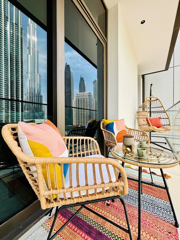 Un balcón con mobiliario de mimbre, una mesa de cristal y vistas a edificios altos.